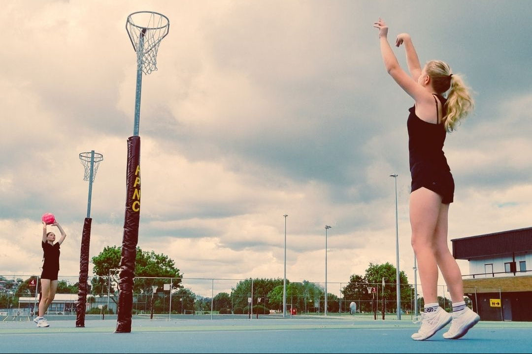 2 netballers practicing shooting hoops at the netball courts both wearing shoot bamboo netball socks